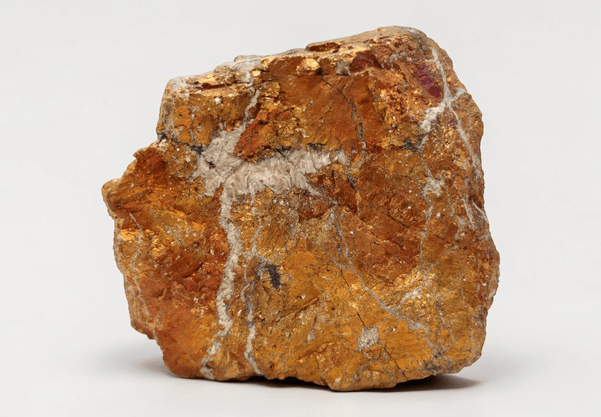 Surowy kawałek miedzianej rudy z widocznymi żyłami minerałów na jasnym tle.