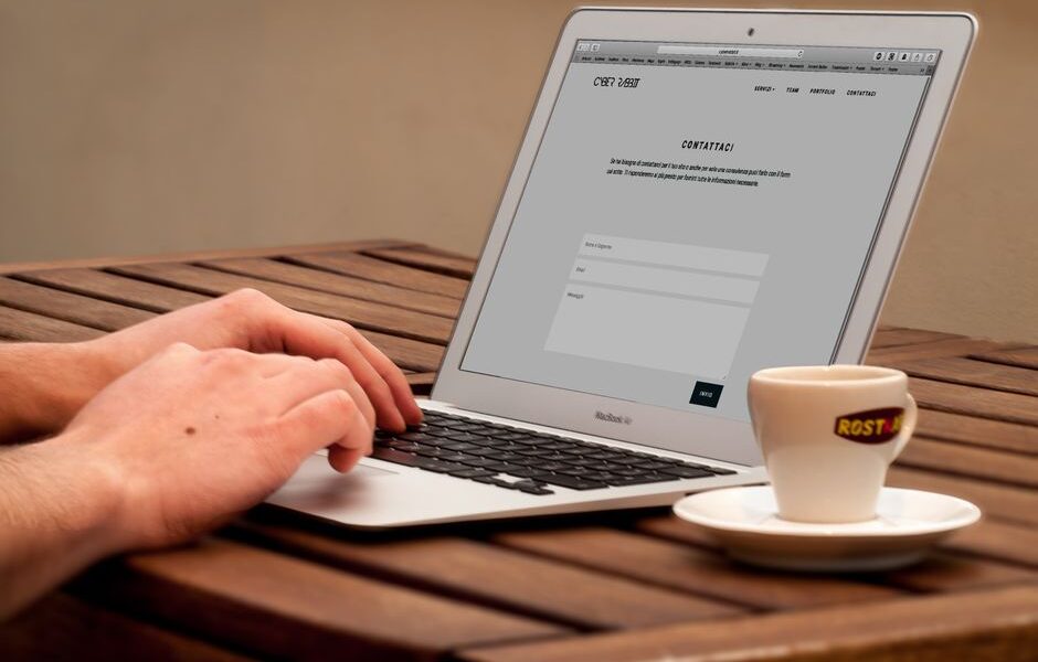 Osoba wypełniająca formularz kontaktowy na laptopie przy filiżance kawy.