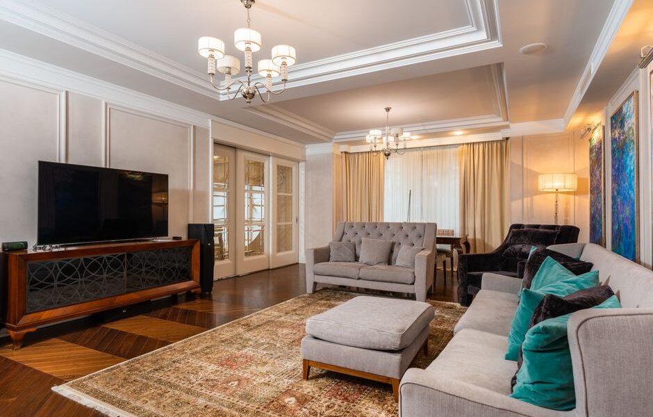 Elegancki salon z szarymi sofami, wzorzystym dywanem i klasycznymi żyrandolami.