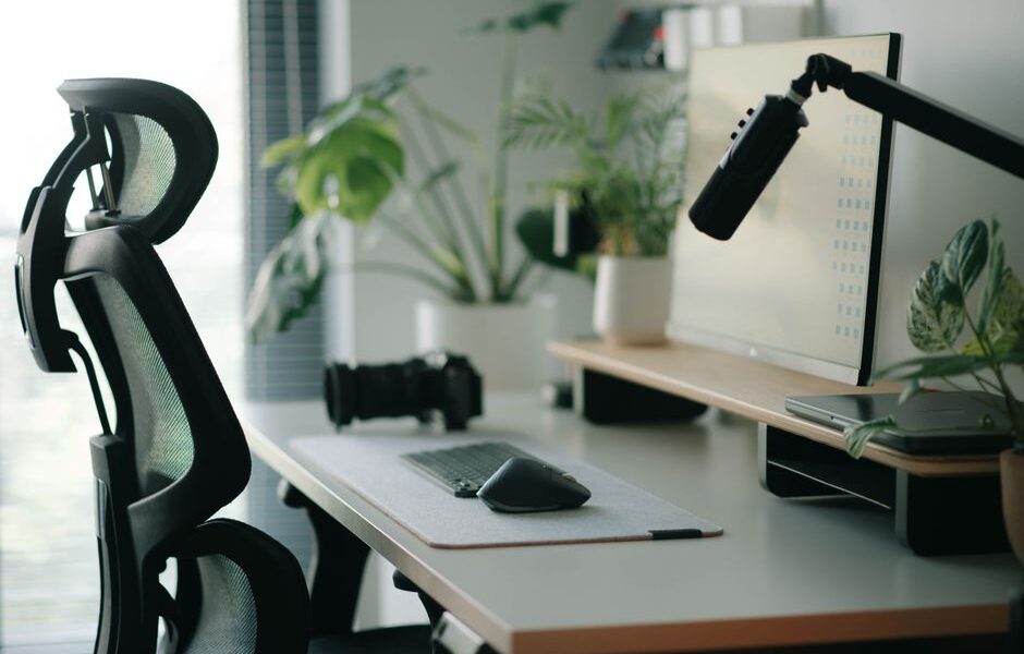 Ergonomiczne krzesło biurowe przy biurku z monitorem, klawiaturą i roślinami doniczkowymi.