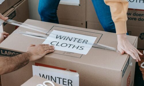 Osoby zaklejają taśmą kartonowe pudło z napisem Winter Cloths