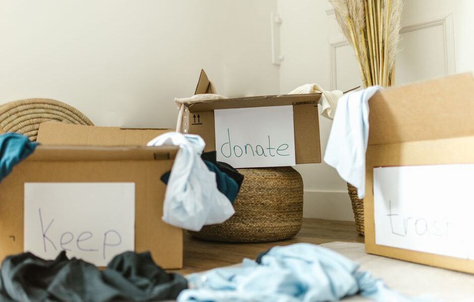 Kartonowe pudła z napisami Keep, donate i trash oraz ubrania